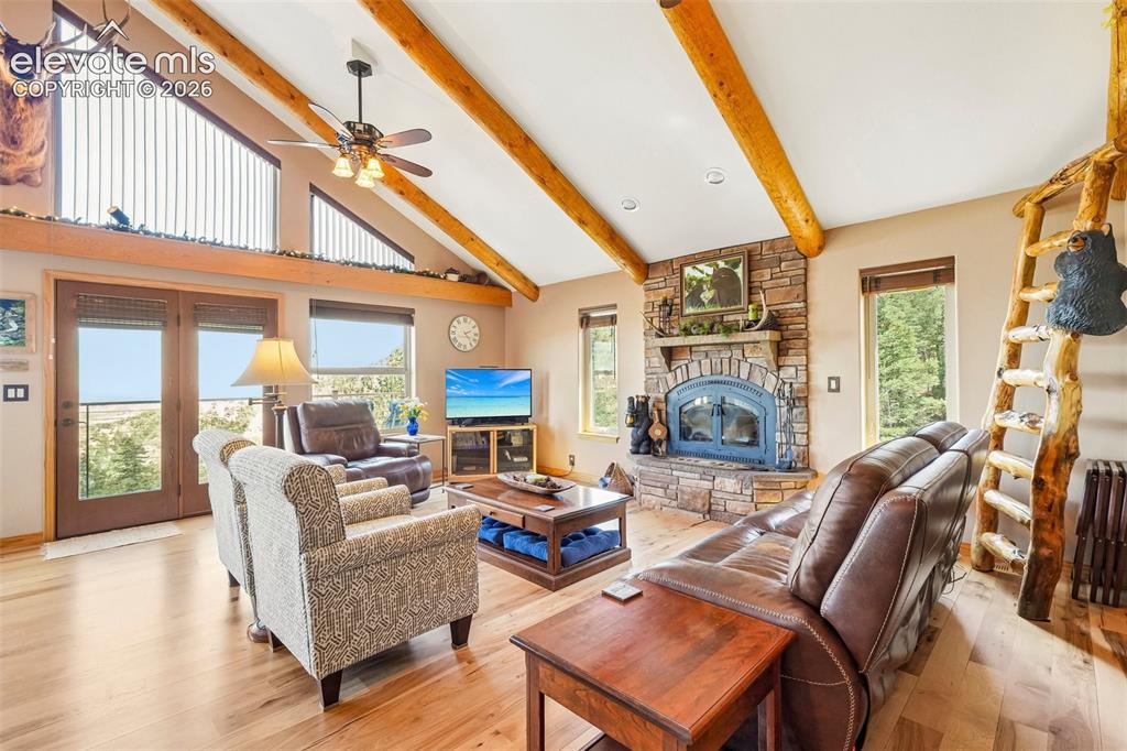 Image 12 of 50: Open concept living room with tall vaulted-wood beamed ceilings, a wood bur