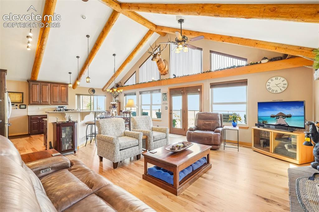 Image 13 of 50: Open concept living room with tall vaulted-wood beamed ceilings, a wood bur
