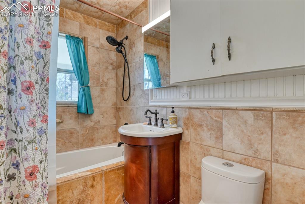 Image 17 of 47: Full bathroom with toilet, tiled shower / bath combo, and tile walls