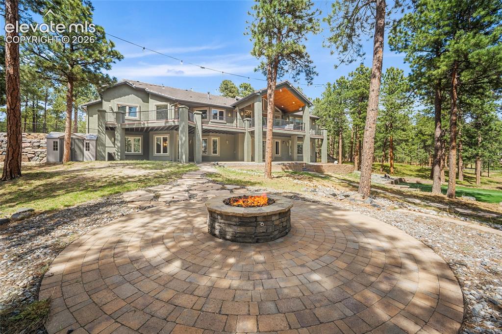 Image 20 of 42: Expansive paver patio with a built-in stone fire pit, surrounded by mature