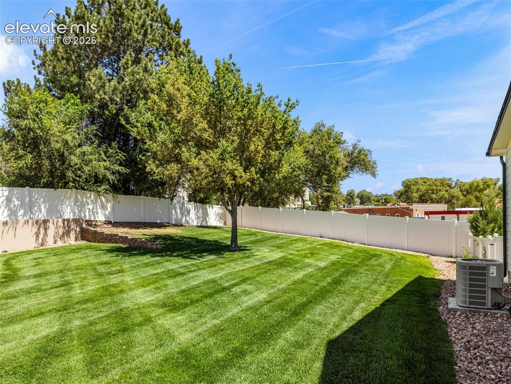 Image 3 of 9: Expansive backyard featuring a lush lawn, white privacy fencing, mature tre