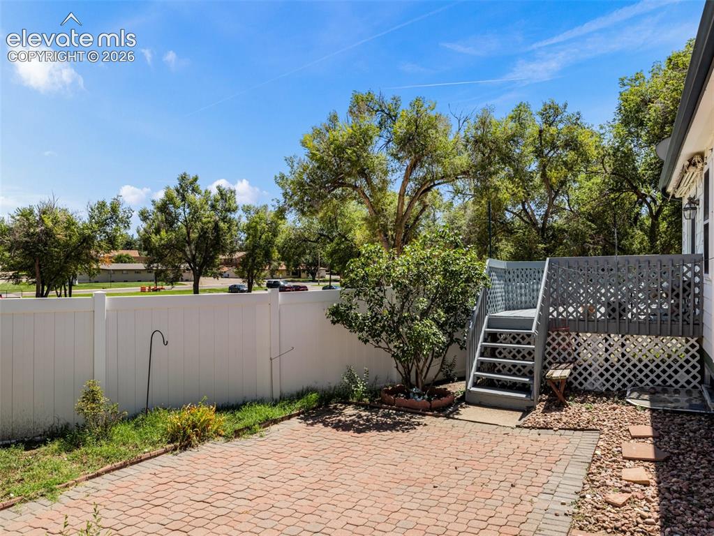 Image 4 of 9: Elevated deck with lattice skirting, paver patio, white vinyl fencing, and 