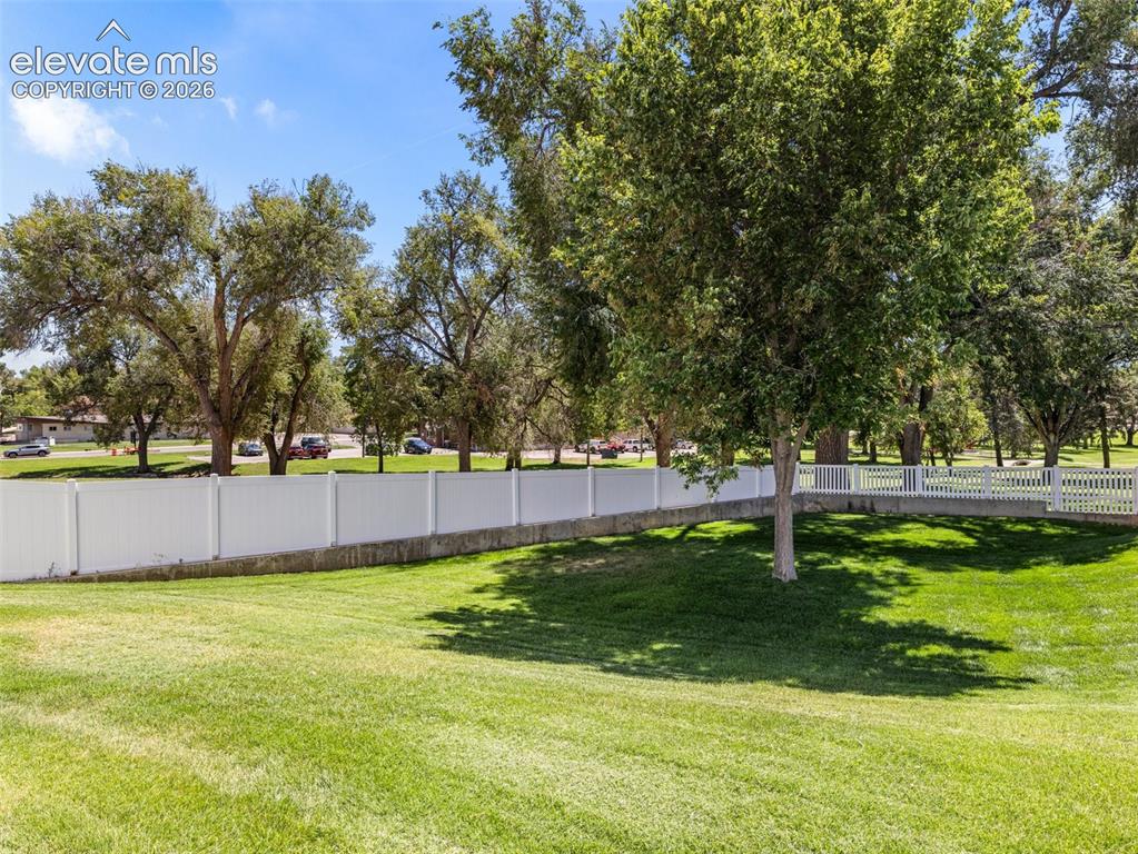 Image 6 of 9: Expansive green lawn with mature trees and a white privacy fence