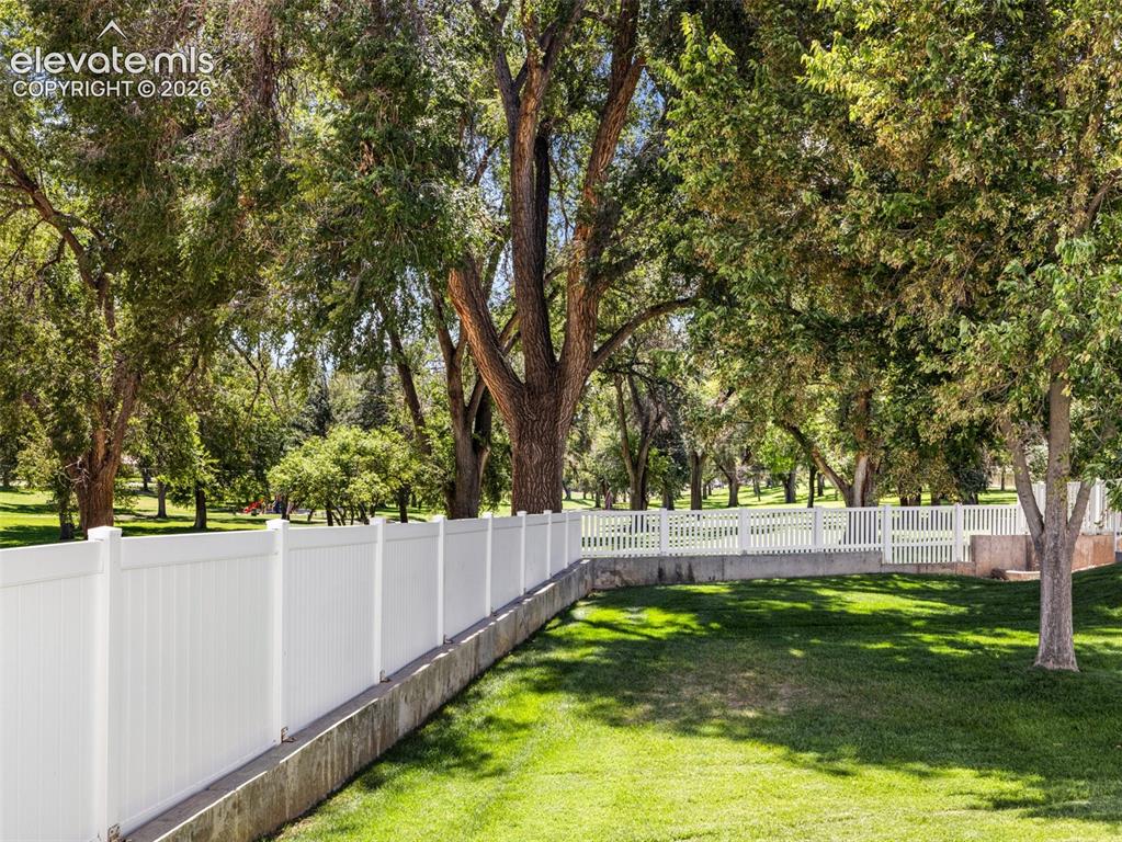 Image 7 of 9: Expansive grassy area with mature trees, featuring a white privacy fence an