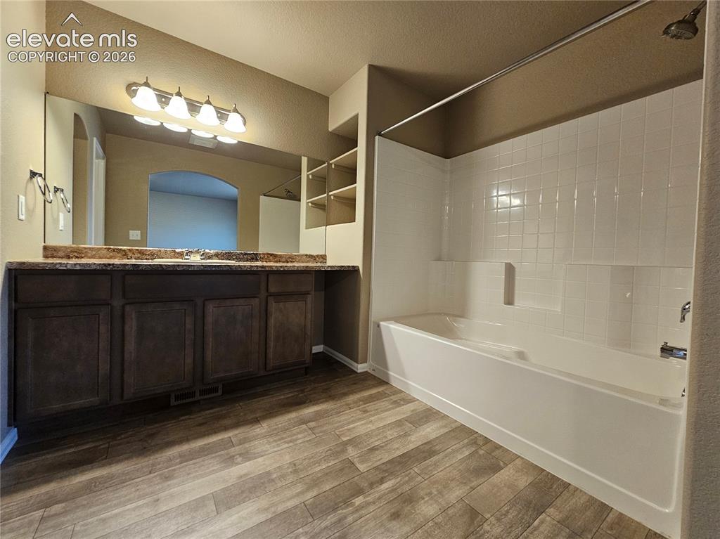 Image 11 of 20: Bathroom featuring wood-finish flooring and a white tile surround bathtub