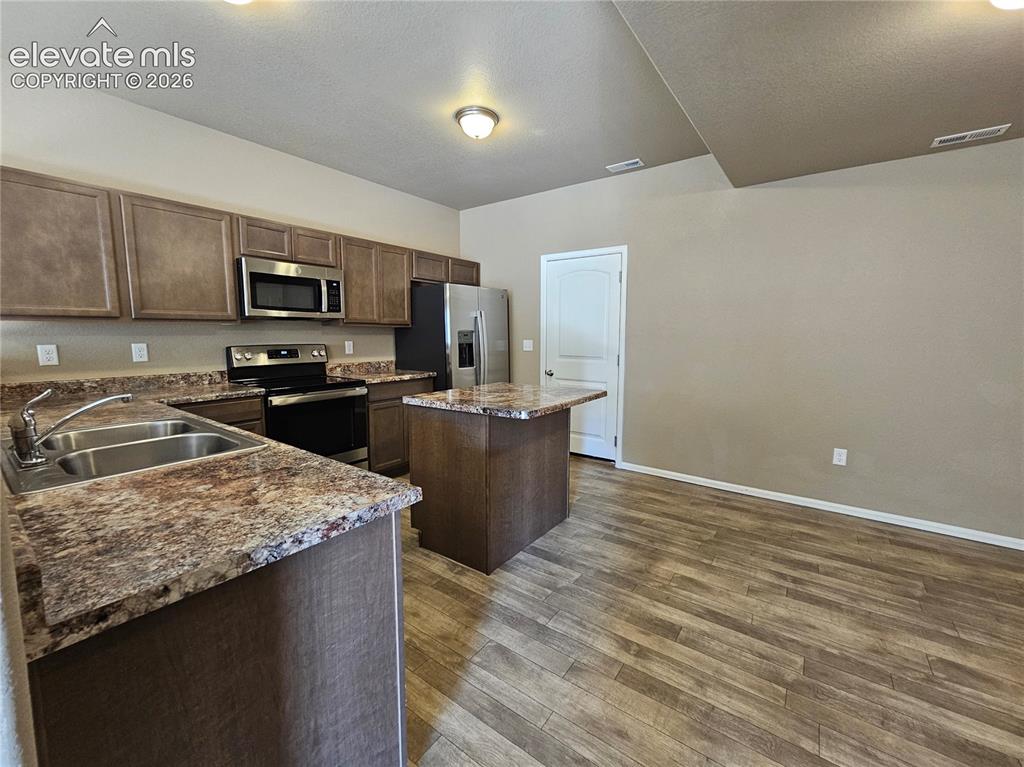Image 6 of 20: Kitchen featuring wood-finish flooring, dark wood cabinetry, and speckled c