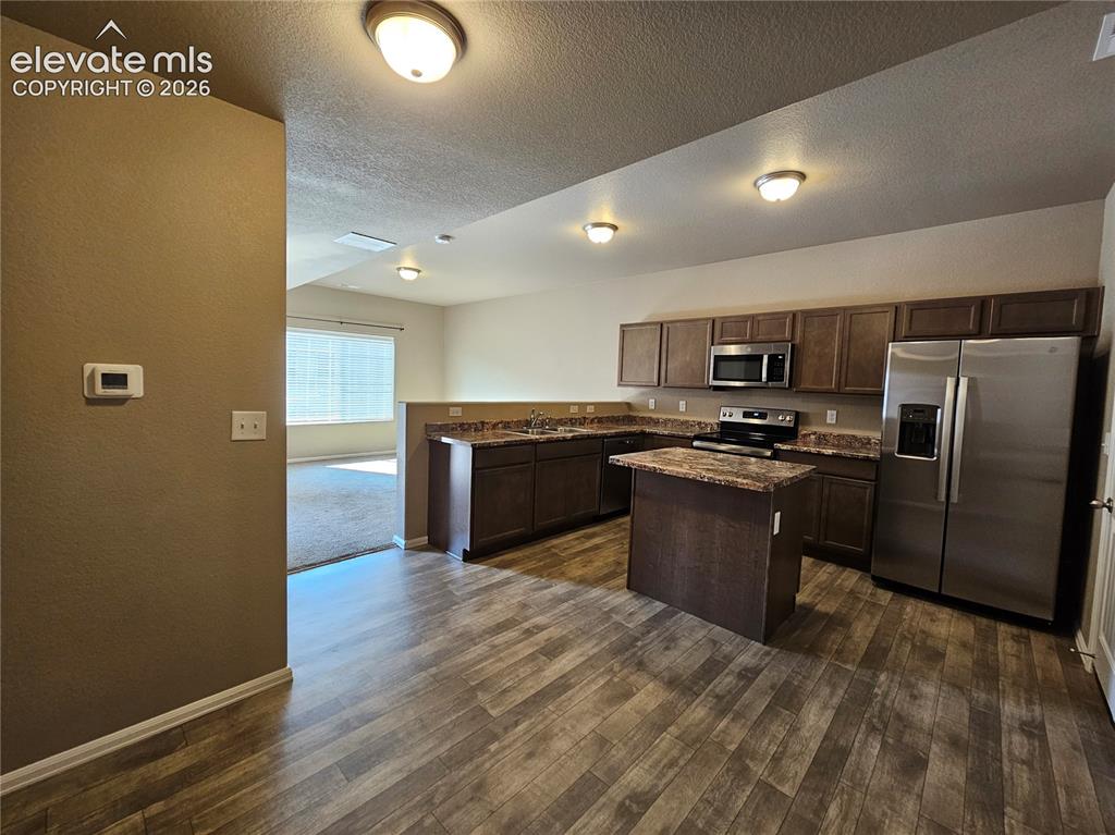 Image 7 of 20: Kitchen featuring wood-finish flooring, dark wood cabinetry, a central isla