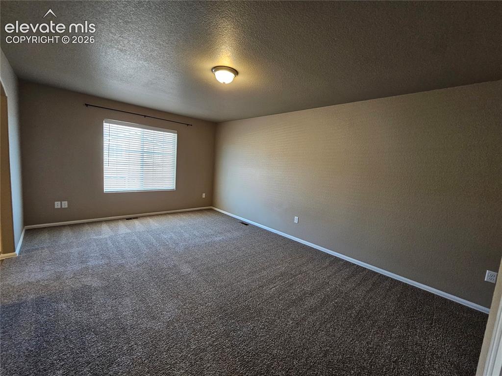 Image 8 of 20: Spacious room featuring neutral-toned walls, textured ceiling, a large wind