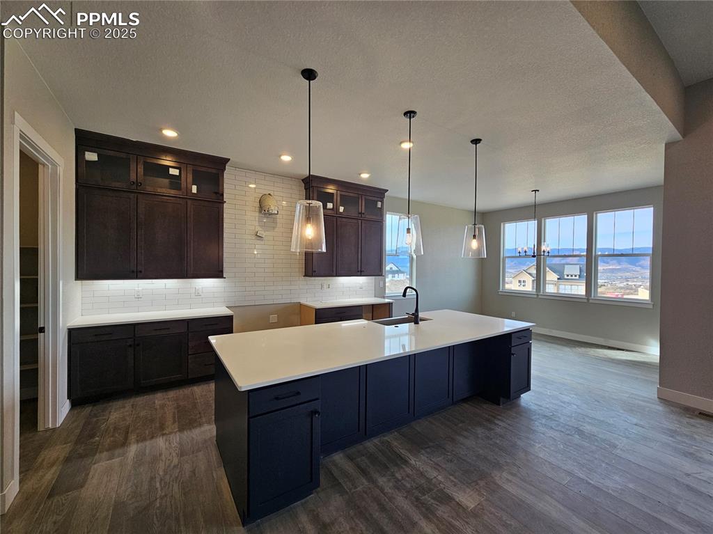 Image 15 of 20: Kitchen with dark brown cabinets, backsplash, glass insert cabinets, pendan