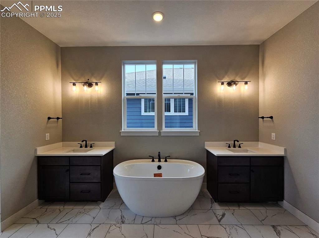 Image 8 of 20: Bathroom with a textured wall, two vanities, a soaking tub, and light marbl