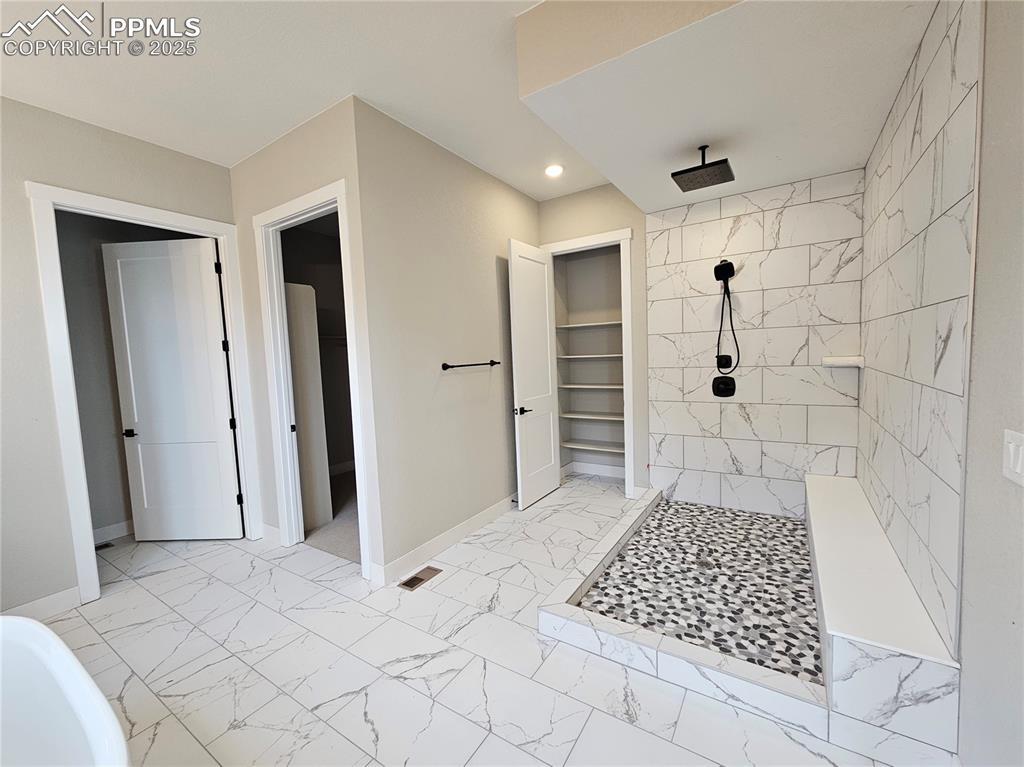 Image 9 of 20: Bathroom with a walk in closet, light marble finish floors, tiled shower, r