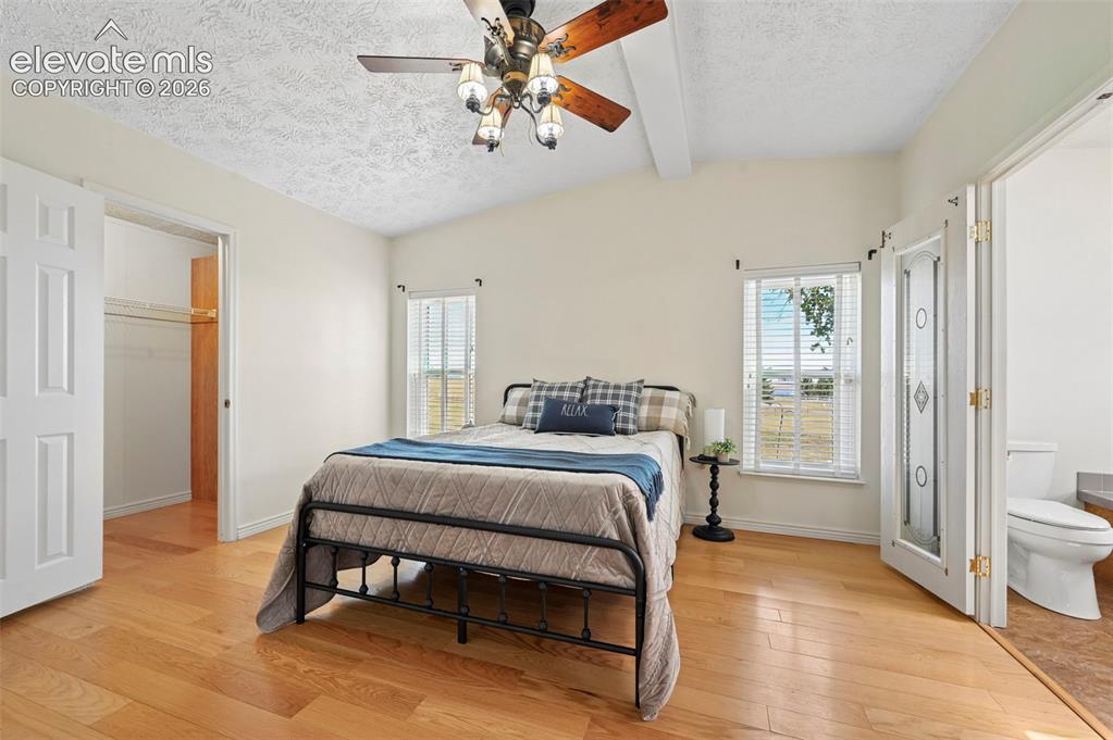 Image 21 of 38: Vaulted ceiling with exposed beam, wood-finish flooring, two windows with b