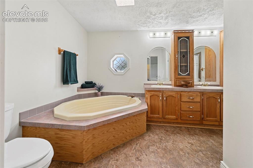 Image 23 of 38: Built-in corner tub with surrounding countertop, dual vanity with wood-fini