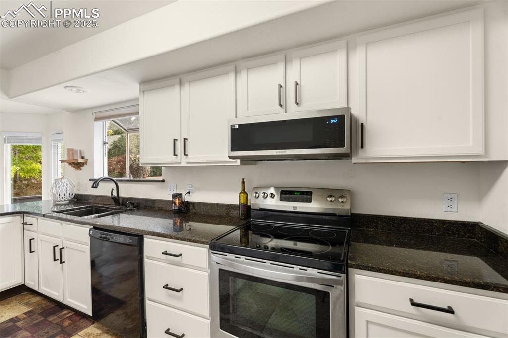 Image 10 of 32: Kitchen featuring stainless steel appliances, white cabinets, and dark ston