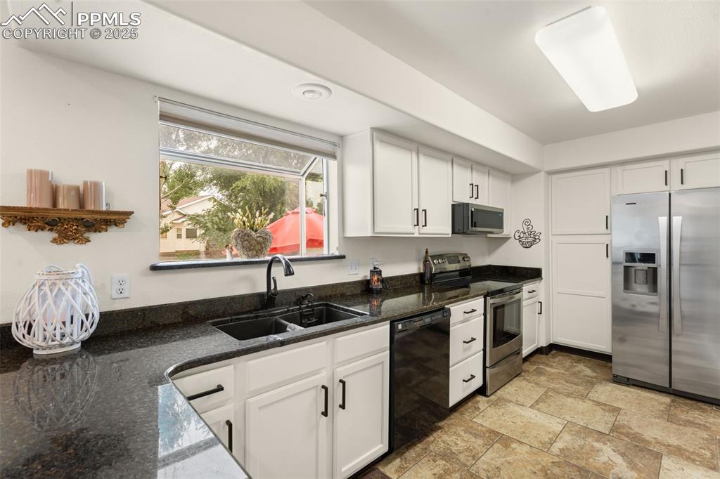 Image 9 of 32: Kitchen with stainless steel appliances, dark stone counters, white cabinet