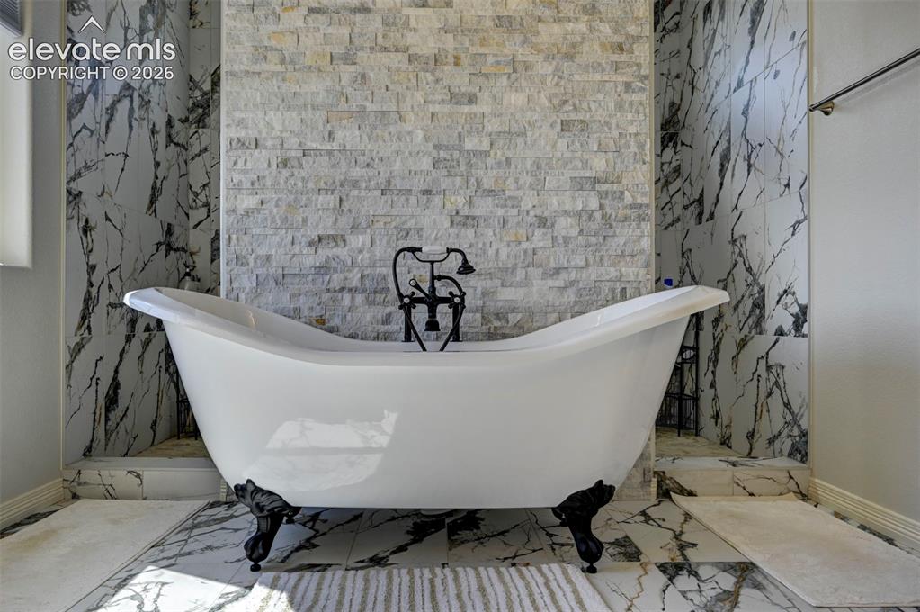 Image 23 of 45: Freestanding clawfoot bathtub with a wall-mounted faucet, set against a sta