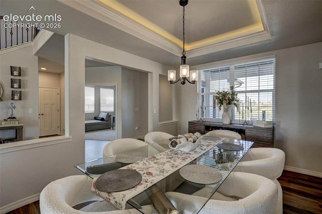 Image 6 of 45: Dining area featuring a glass-top table, a contemporary chandelier, and tra