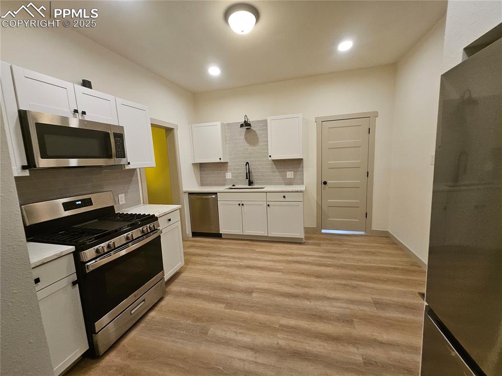 Image 16 of 23: Kitchen with appliances with stainless steel finishes, white cabinets, ligh