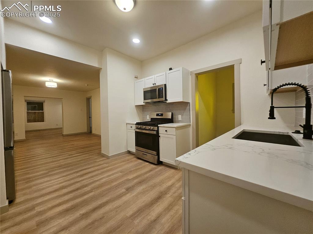 Image 18 of 23: Kitchen with stainless steel appliances, light wood-style flooring, backspl