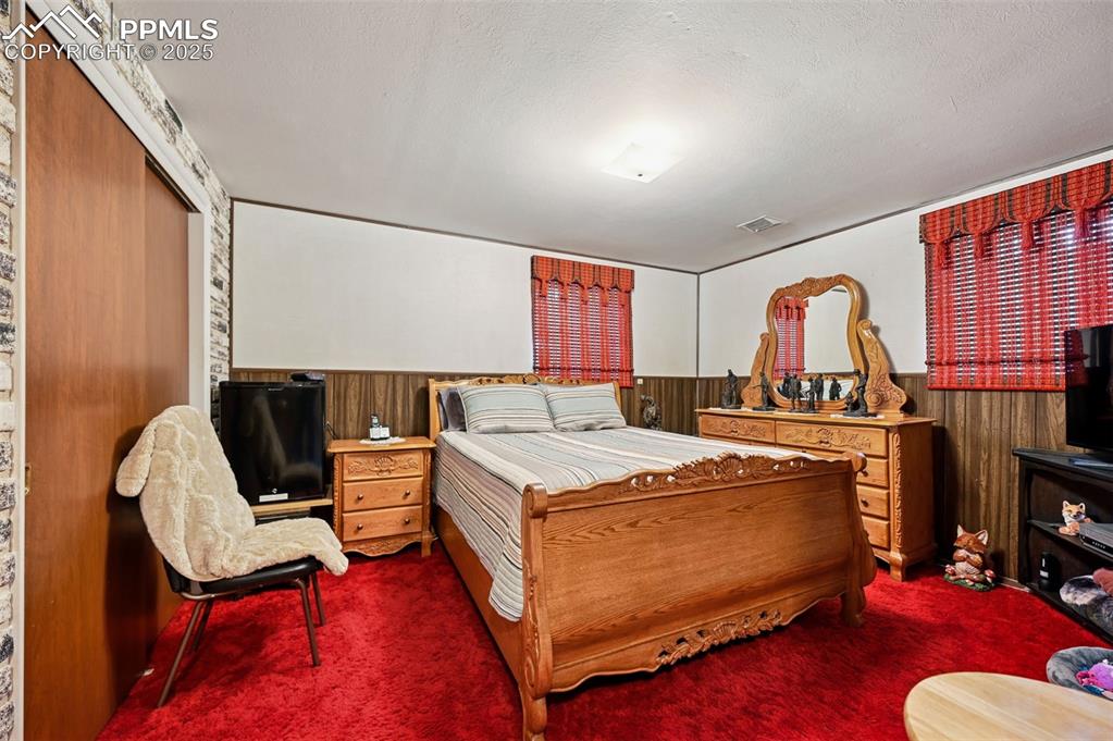 Image 16 of 23: Carpeted bedroom with wood walls, a wainscoted wall, and a textured ceiling