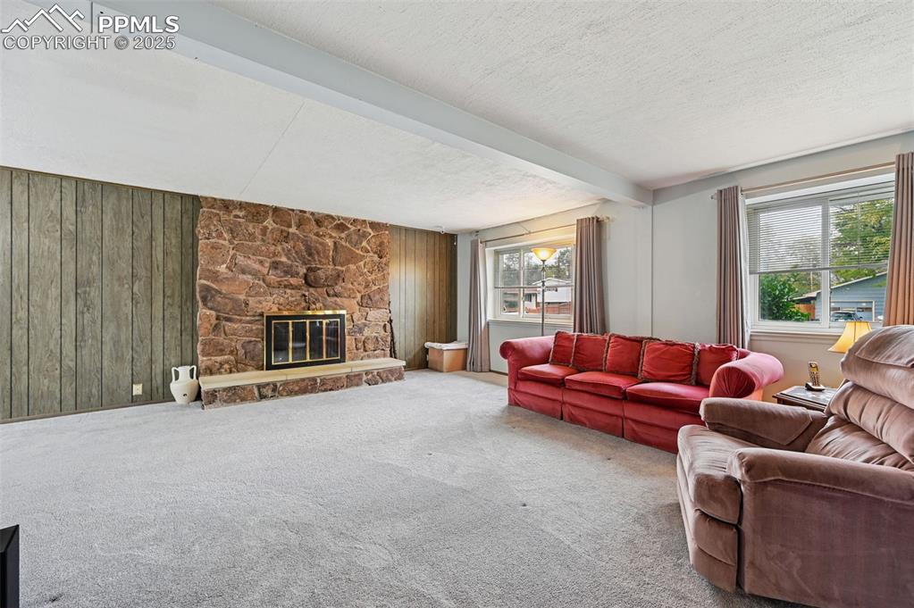 Image 3 of 23: Living room with beam ceiling, carpet, a stone fireplace, wooden walls, and