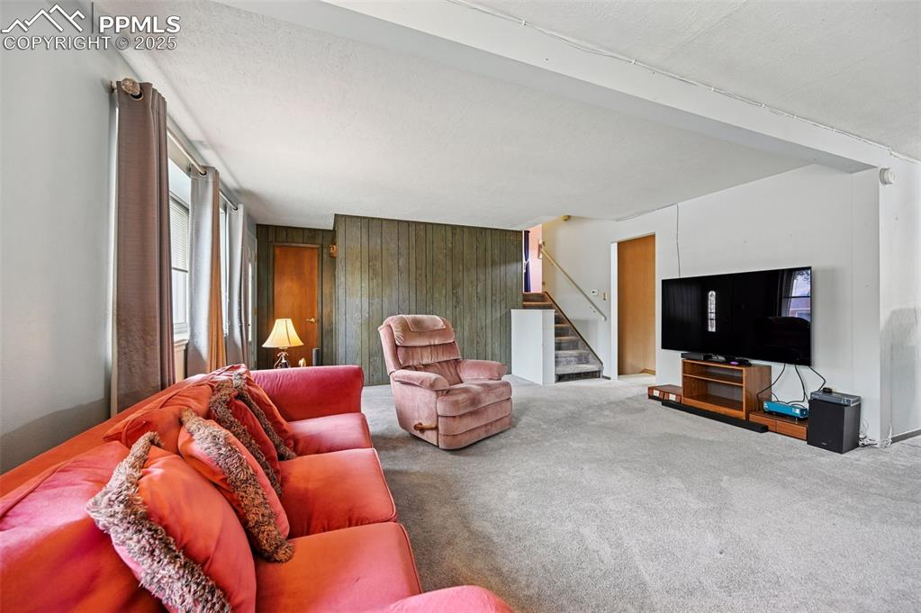 Image 5 of 23: Living room with wooden walls, carpet flooring, and stairs