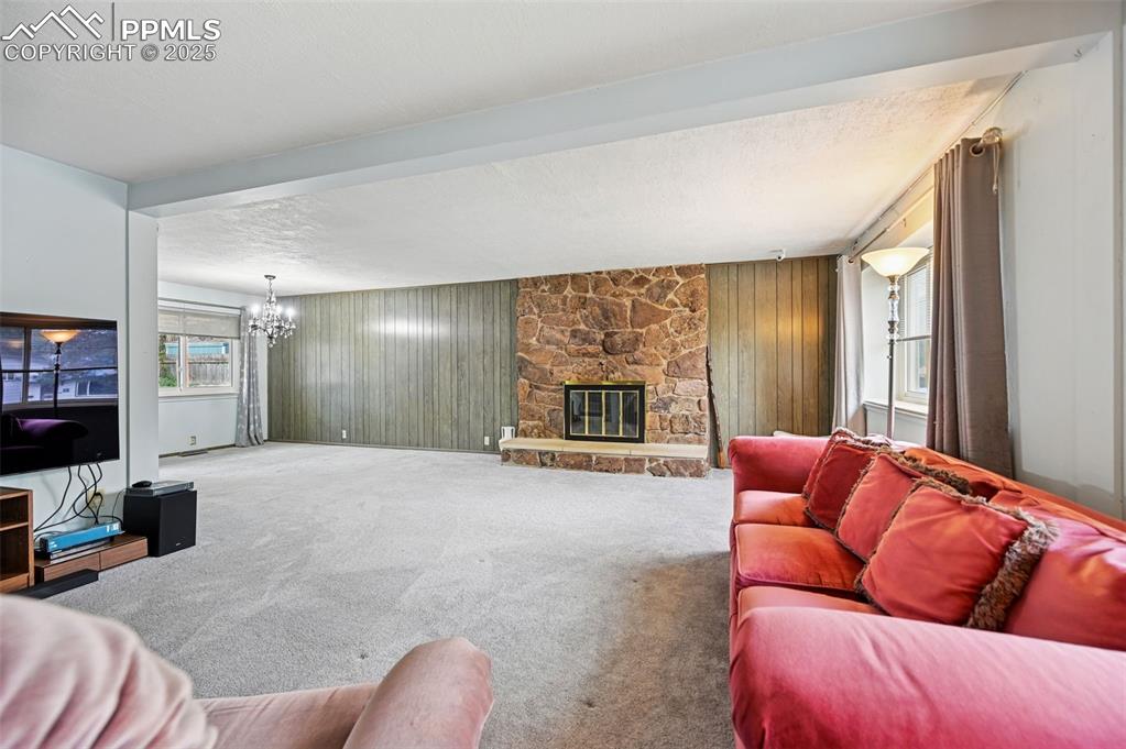 Image 7 of 23: Carpeted living area featuring a stone fireplace, wood walls, a textured ce