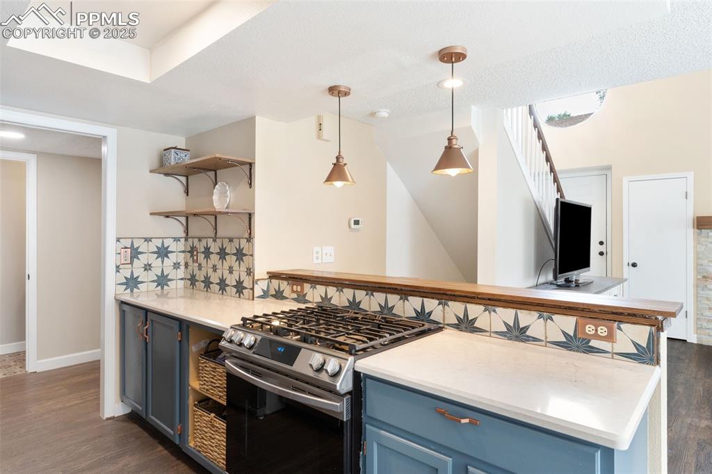 Image 13 of 34: Kitchen with blue cabinets, stainless steel gas stove, a breakfast bar, and