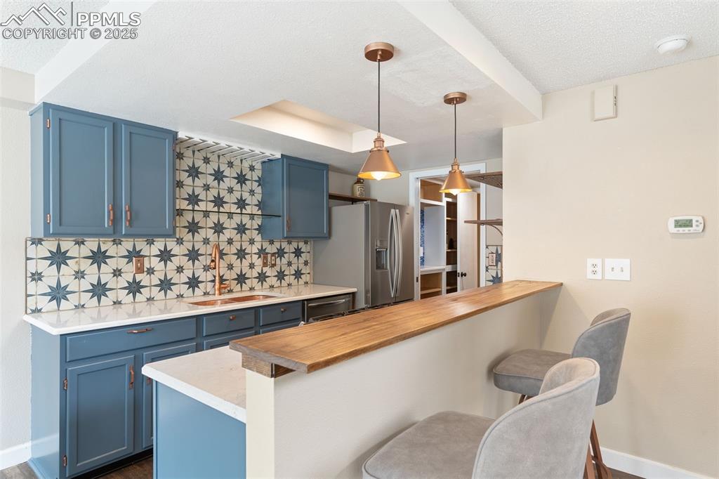 Image 15 of 34: Kitchen featuring blue cabinets, a kitchen breakfast bar, decorative backsp