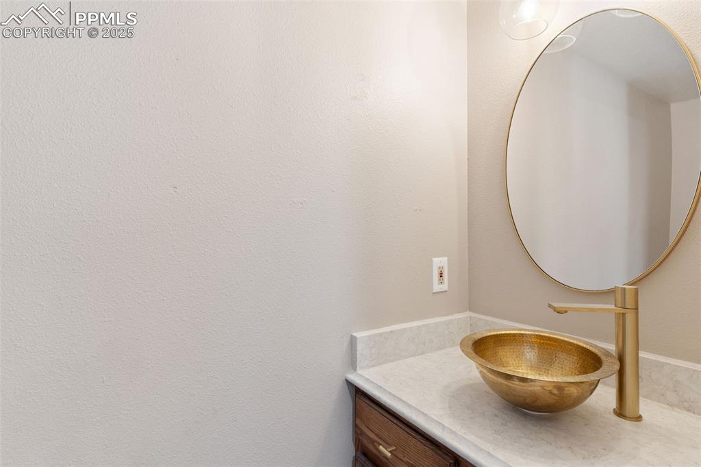 Image 18 of 34: Half bath with vanity and modern brushed gold-look fixture and sink.