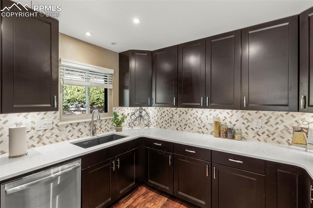 Image 16 of 46: Kitchen featuring dishwasher, backsplash, dark wood finished floors, dark b