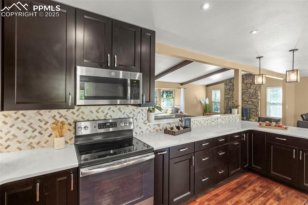 Image 17 of 46: Kitchen with appliances with stainless steel finishes, backsplash, dark woo
