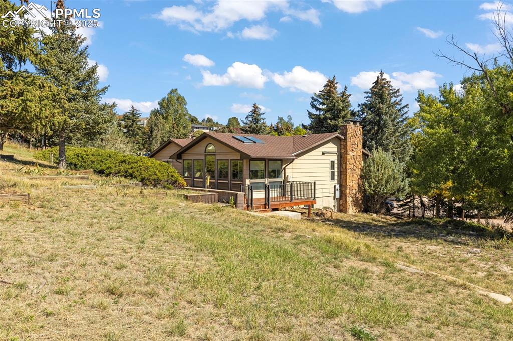 Image 40 of 46: Back of house with a yard, a sunroom, a wooden deck, a chimney, and view of