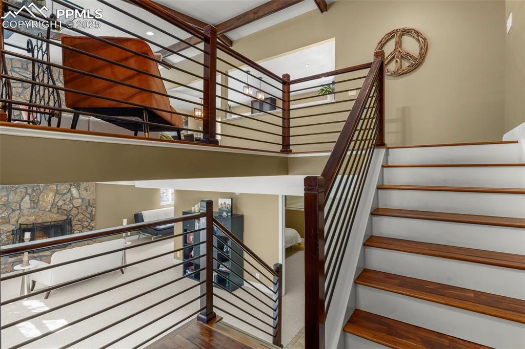 Image 5 of 46: Stairs featuring a stone fireplace, wood finished floors, a high ceiling, a