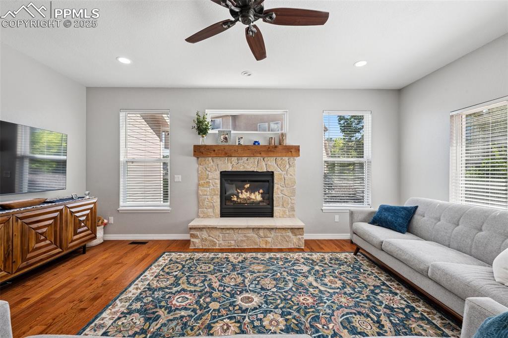 Image 13 of 50: Living area featuring wood finished floors, a stone fireplace, a ceiling fa