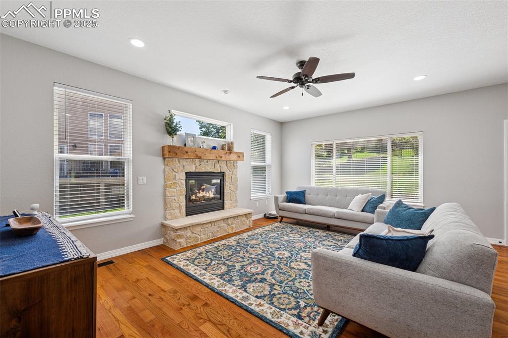 Image 14 of 50: Living area with a ceiling fan, wood finished floors, a stone fireplace, an