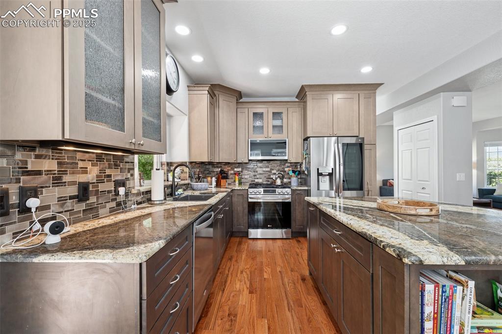 Image 8 of 50: Kitchen with stainless steel appliances, light wood finished floors, glass