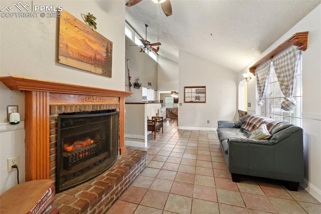 Image 11 of 38: Living room with vaulted ceiling, ceiling fan, a textured ceiling, a firepl