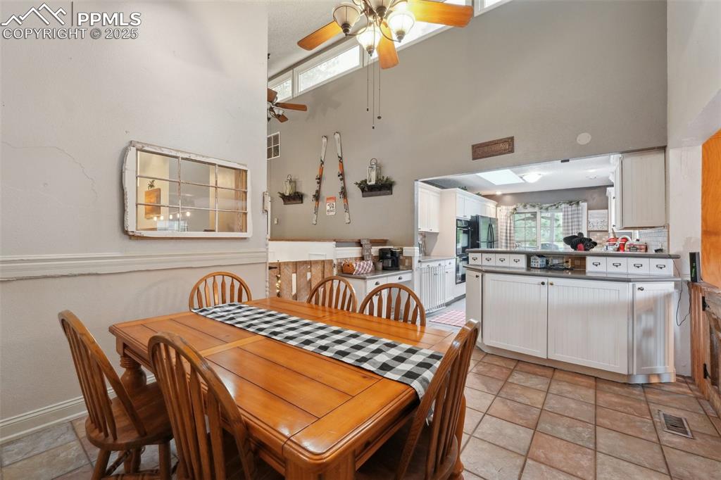 Image 13 of 38: Dining area featuring a towering ceiling, ceiling fan, and light stone fini