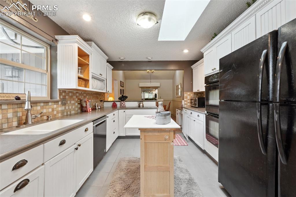 Image 14 of 38: Kitchen featuring black appliances, a sink, a skylight, backsplash, and a k