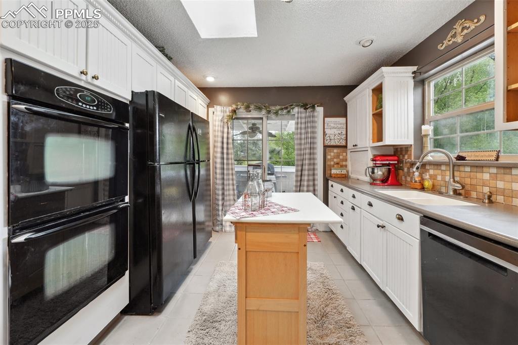 Image 15 of 38: Kitchen featuring black appliances, a sink, white cabinets, tasteful backsp
