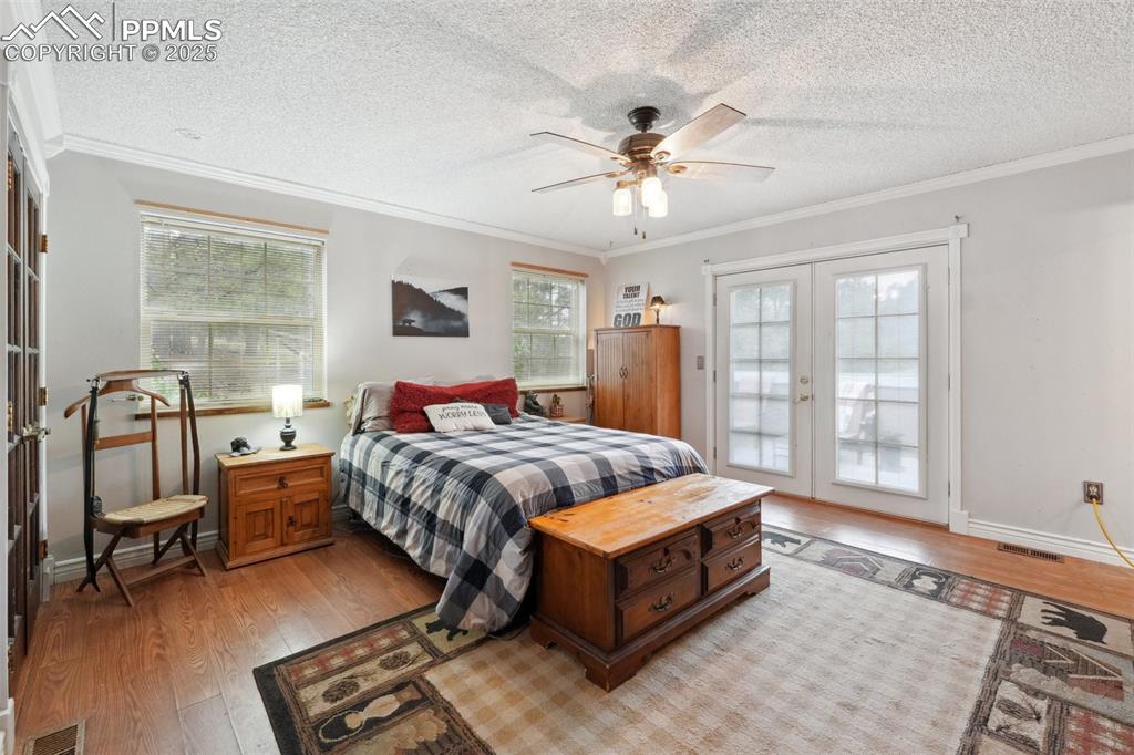 Image 18 of 38: Bedroom with french doors, light wood finished floors, multiple windows, ac