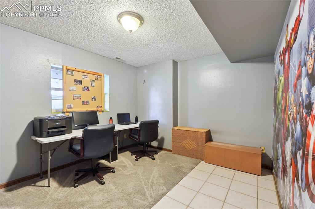 Image 23 of 38: Carpeted home office with a textured ceiling, tile patterned flooring, and 