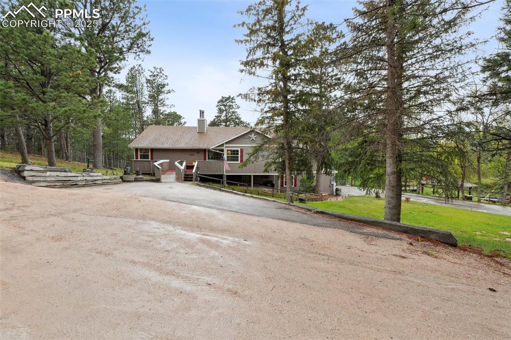 Image 30 of 38: View of front of home with driveway, a chimney, and a wooden deck