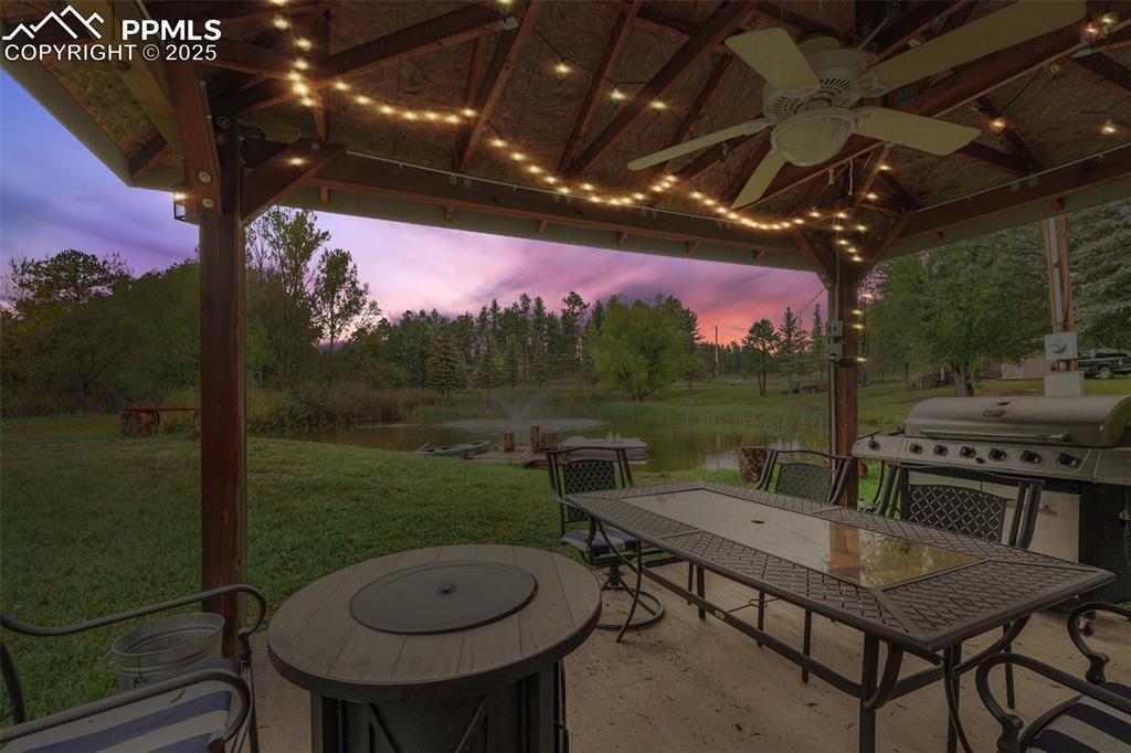 Image 7 of 38: Patio terrace at dusk with a water view, outdoor dining space, a yard, a ce