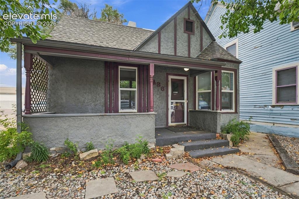 Caption: Stucco exterior with decorative trim, covered front porch, lattice detailing, and a shingled roof