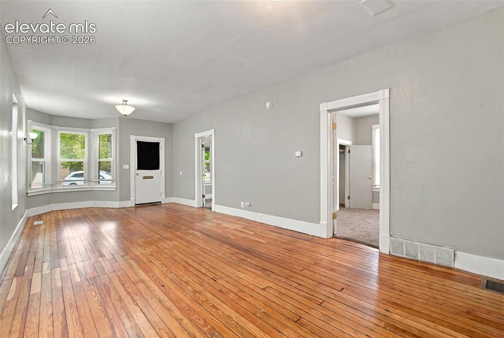 Image 13 of 34: Hardwood flooring, bay window, white trim, and a semi-flush mount ceiling l