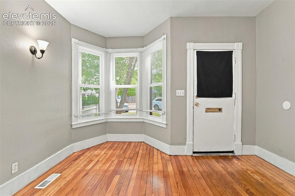 Image 15 of 34: Bay window with white blinds, sconce lighting, wood-finish flooring, and a 