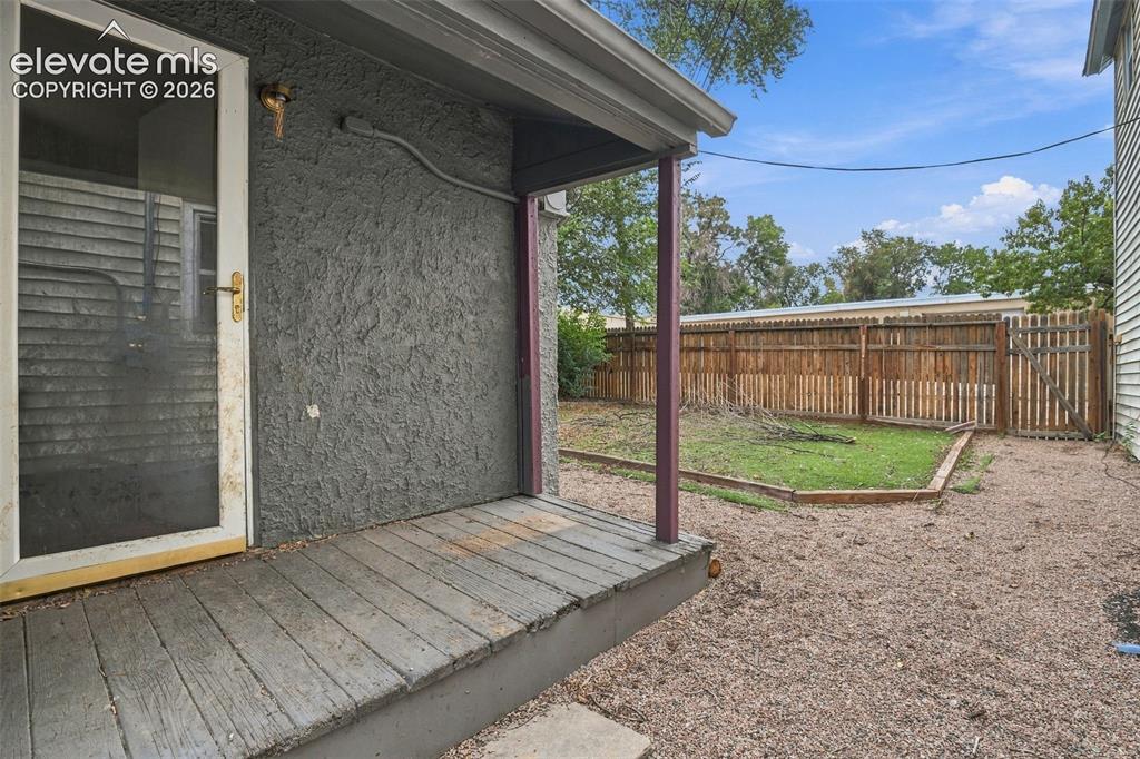 Image 24 of 34: Rear porch with a wooden deck, stucco exterior, and a privacy fence enclosi