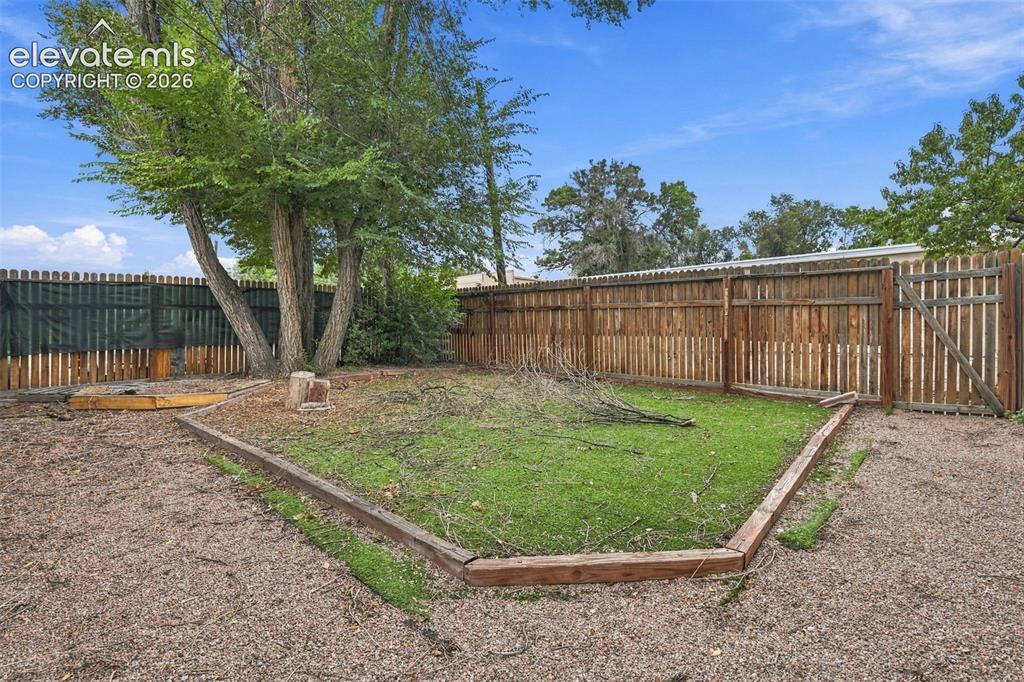 Image 25 of 34: Enclosed backyard featuring a wood fence, mature tree, and a grass area